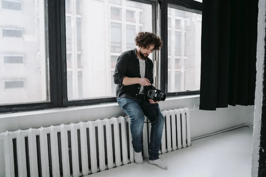 Photographer sitting by a studio window, reviewing a camera between shoots