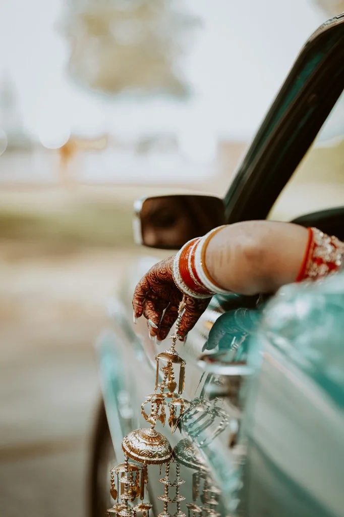 Bride with henna and bangles resting her hand from a car window, holding ceremonial jewelry